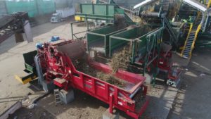 A Rotochopper B-66 E grinder machine being filled with organic material by other machines in an outdoor area.