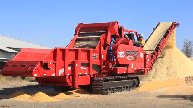 A large Rotochopper B-66 grinding machine depositing finely-ground high-moisture corn in a large pile at a farm site.