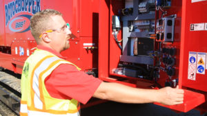 A man opening the inside panel of a large Rotochopper machine where controls and buttons are located.