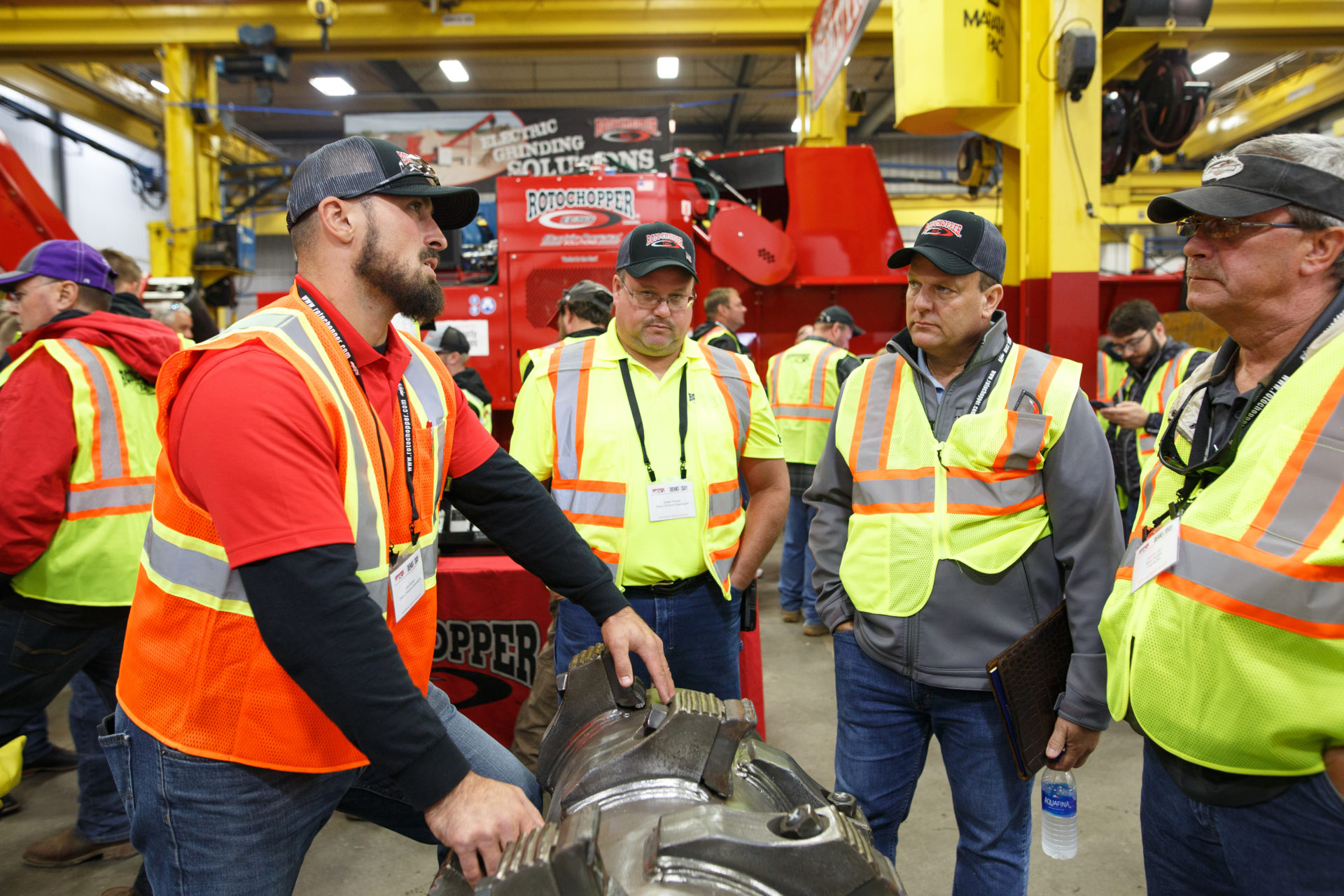 Man demonstrating large rotor component of a grinding machine to other men during Rotochopper's demo day event.