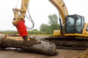 A big machine is using a screw splitter to split a part of a tree trunk laying on the ground at the demo day event.