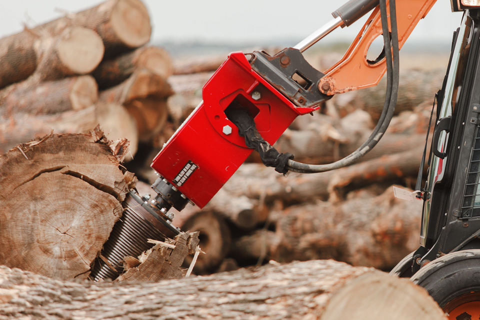 A screw splitter is shown drilling into a large tree trunk on the ground, breaking it apart.