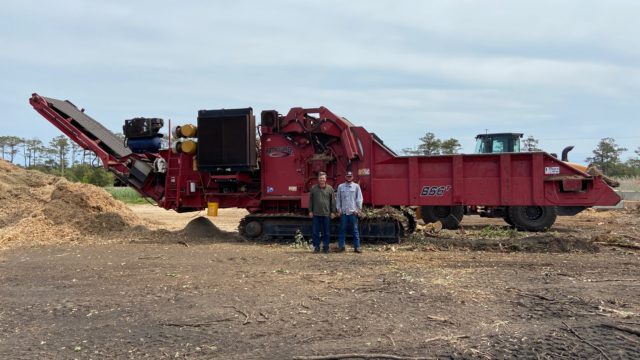 Two men standing in front of a large, red, tracked Rotochopper B-66T mulch-grinding machine