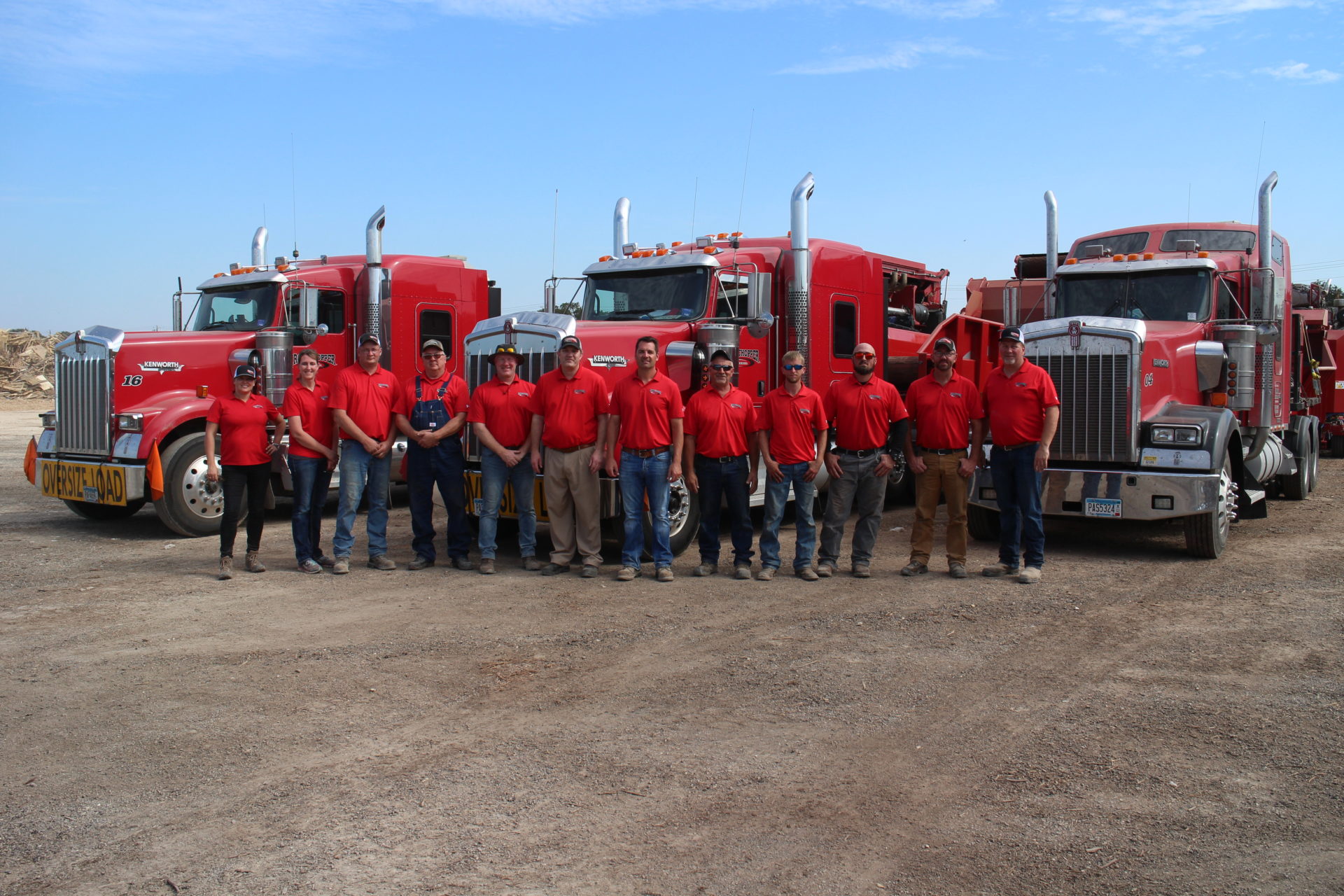 Group of Rotochopper employees pose for a photo together in front of three semi trucks outdoors.
