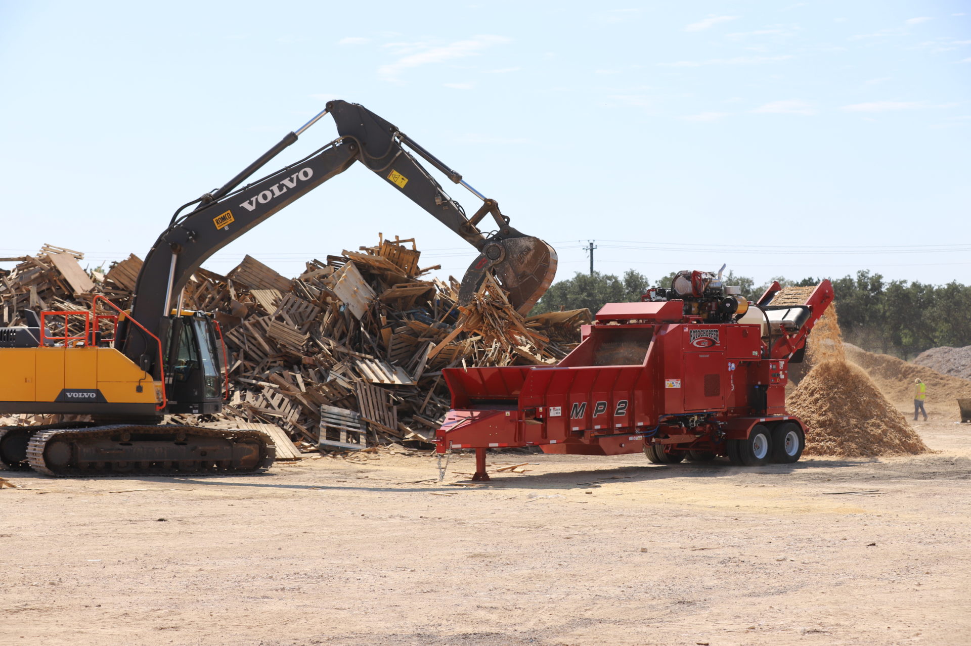 Excavator placing debris to be ground up in a Rotochopper grinding machine at Rotochopper Texas Field Day.