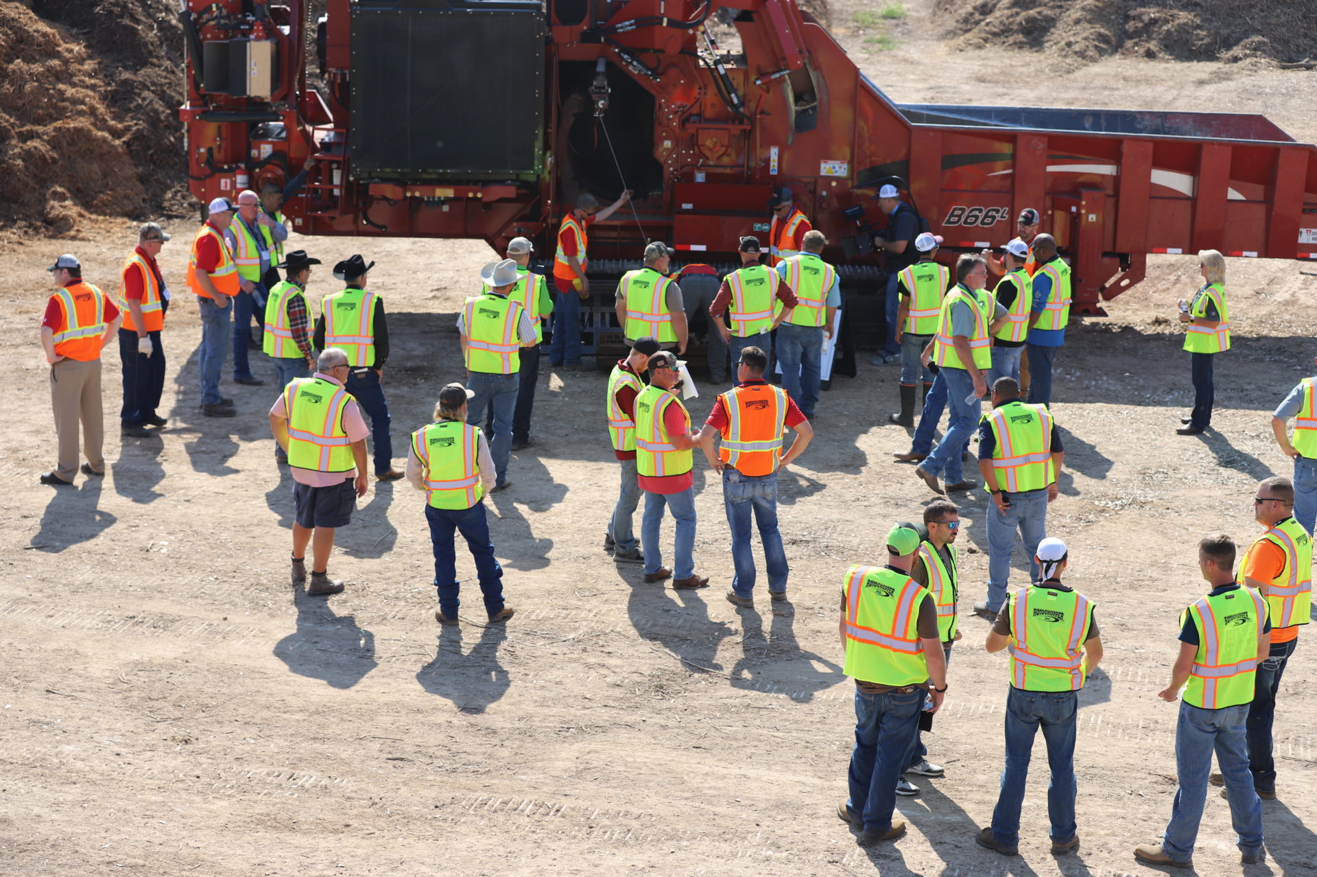 Crowd of men wearing safety vests surrounding a large horizontal grinder at Rotochopper's field day event.