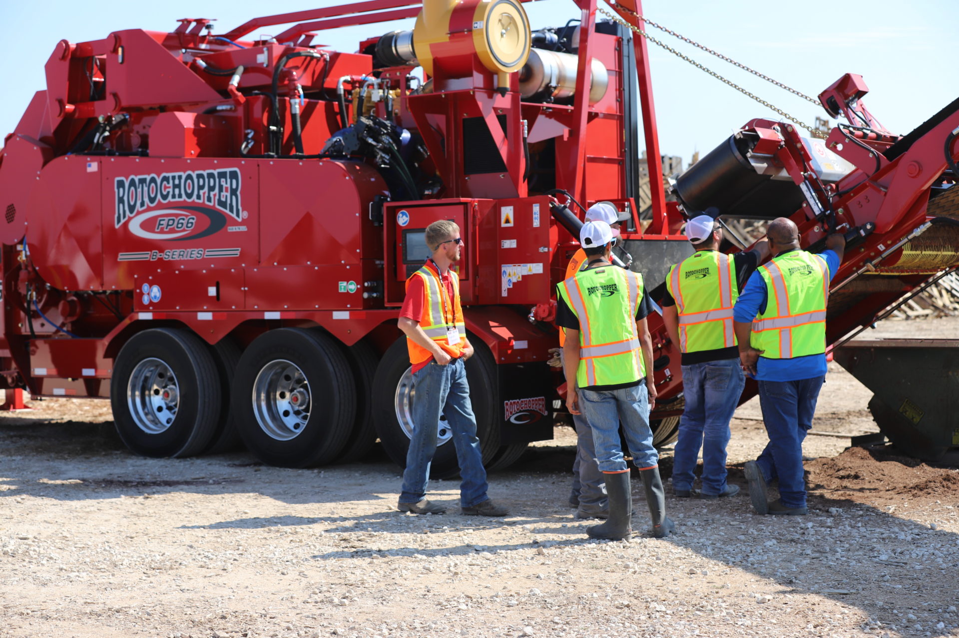 Large group of men with safety vests surrounding a large grinding machine at Rotochopper's field day event.