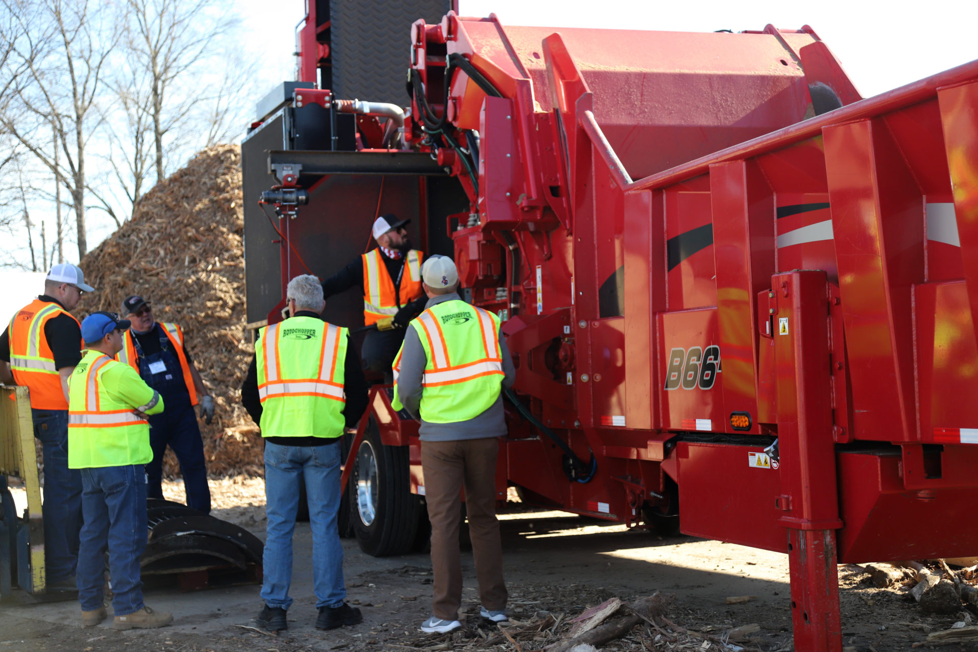 Group of men with safety vests surrounding a large grinding machine for a demo at Rotochopper's field day event.