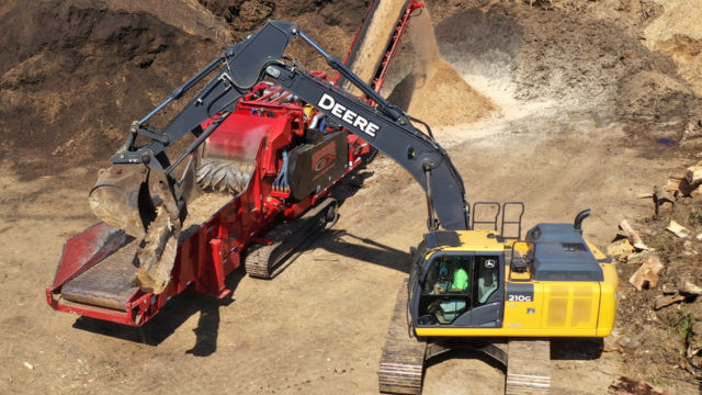 A Rotochopper horizontal grinder being mechanically loaded with logs.