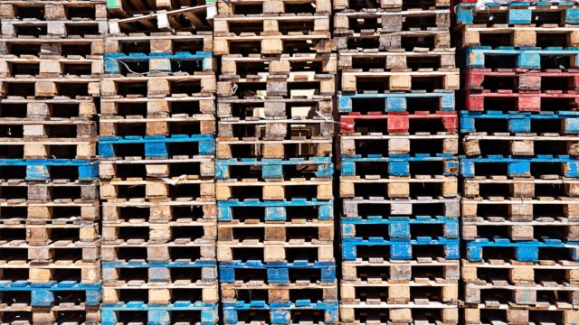 Wooden pallets of various colors stacked in columns.
