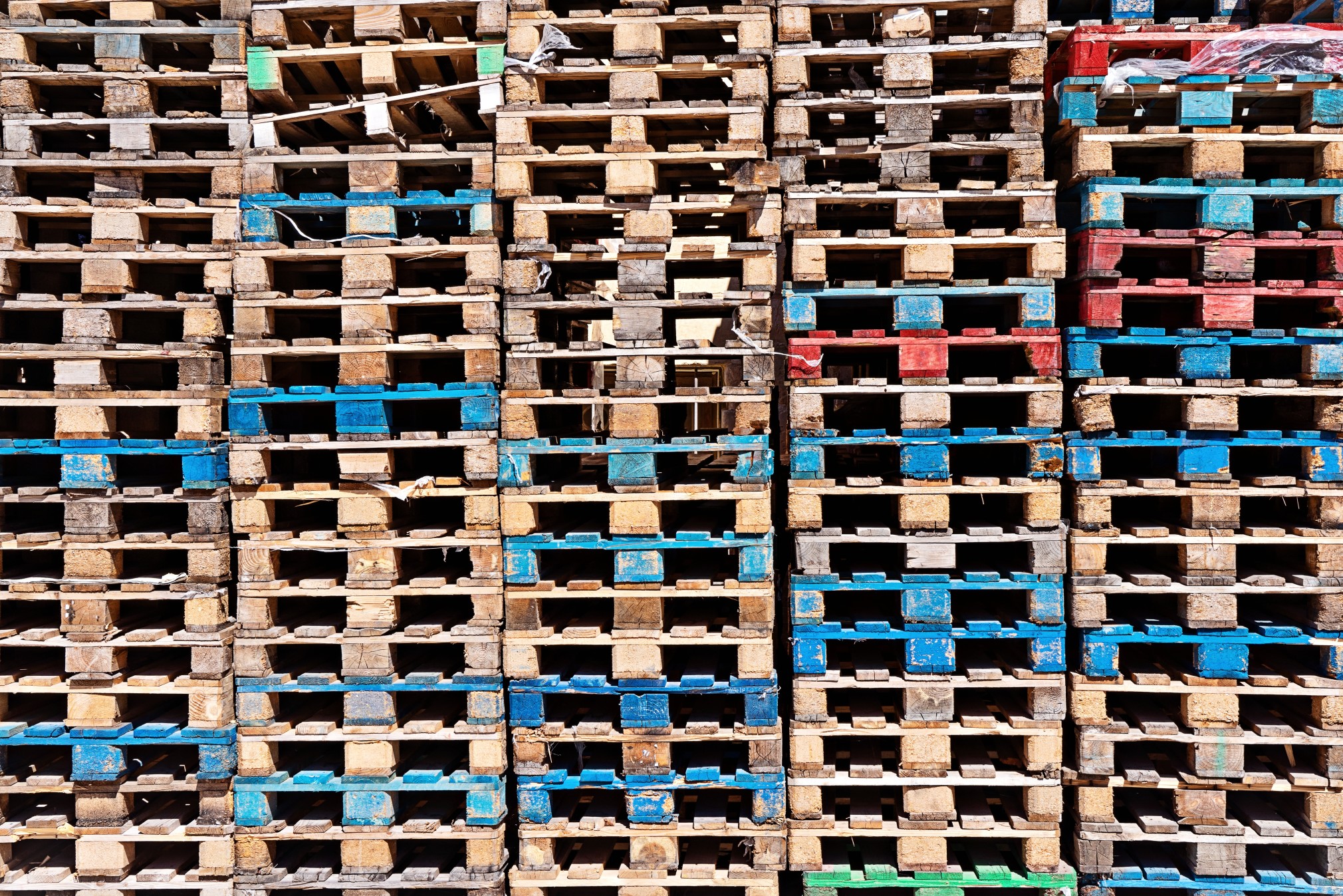 Wooden pallets of various colors stacked in columns.