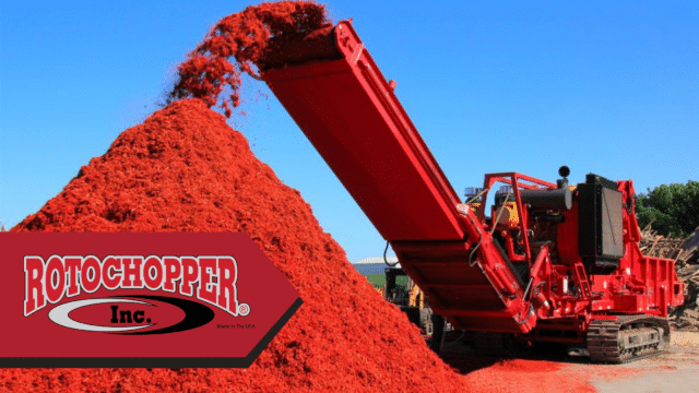 A bright red Rotochopper grinder sits on the right side of a construction site. The grinder is dumping bright red-colored mulch into a pile in front of it. On the bottom left of the photo is the Rotochopper logo.