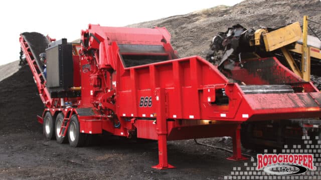 A Rotochopper horizontal grinder processing asphalt shingles. The Rotochopper logo is in the bottom right corner.