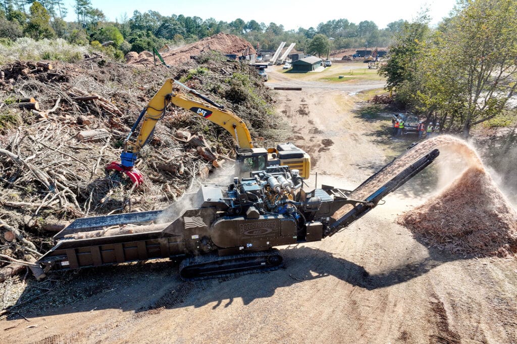 Rotochopper horizontal grinder processing storm debris with excavator feeding woody material into the infeed